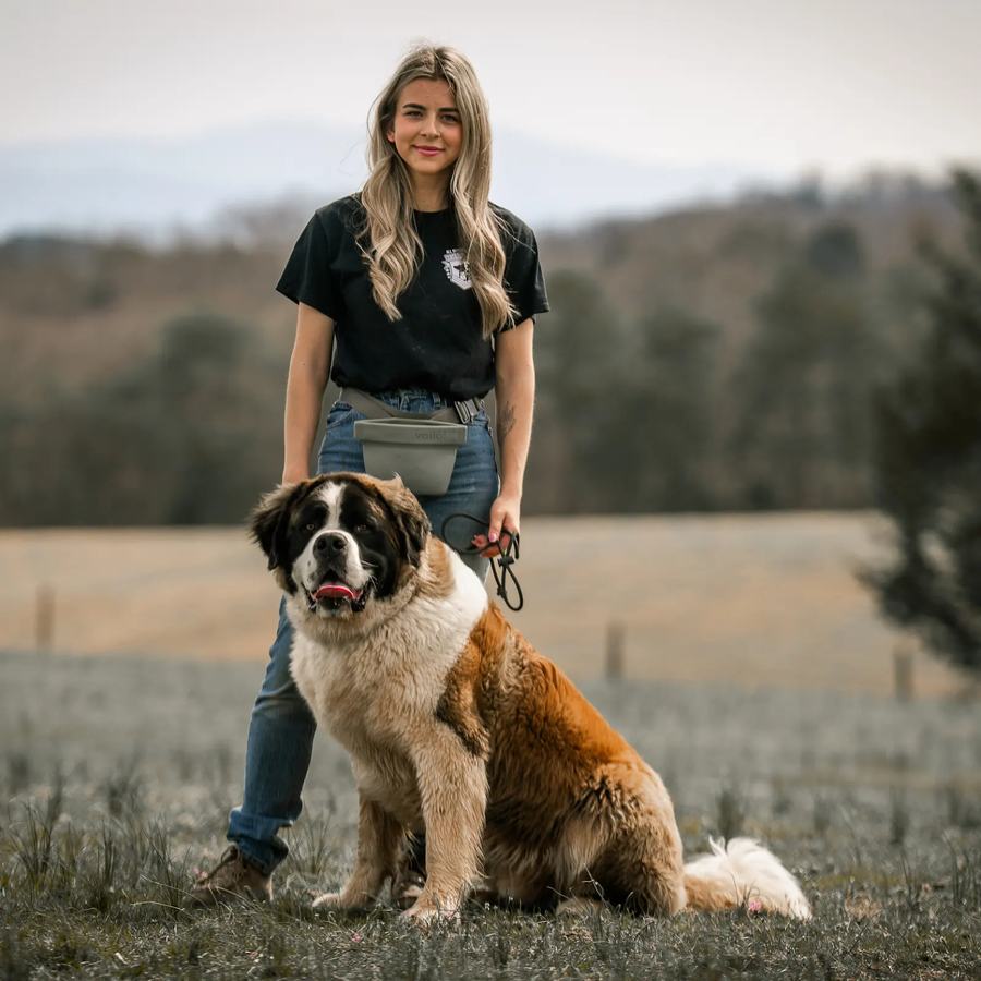 Rebeka standing with her Saint Bernard on a hillside farm